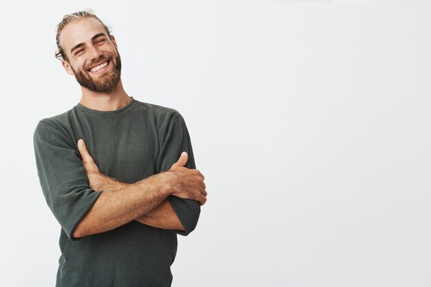 Attractive swedish man with stylish hair and beard laughs with crossed hands and closed eyes.