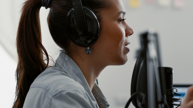 Attractive talk show host broadcasting while talking to audience in home studio. Internet famous star speaking at microphone to public while recording video podcast in living room.