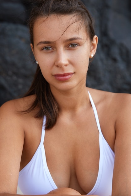 Attractive tanned young female tourist model wears white swimwear