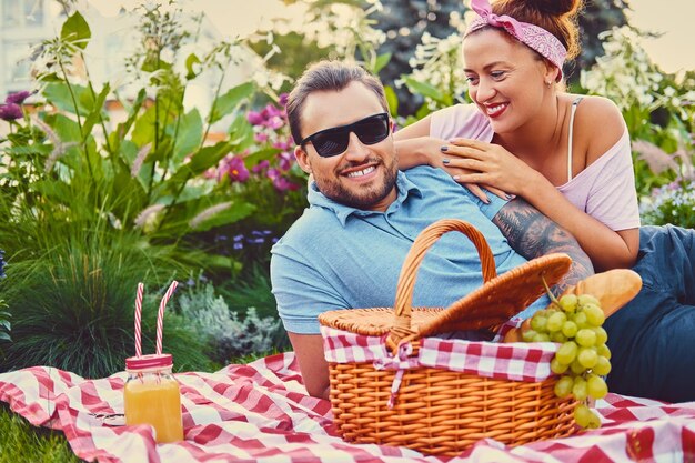 Attractive tattooed, bearded male and a redhead female lying on a blanket on a lawn in a park. Picnic time.