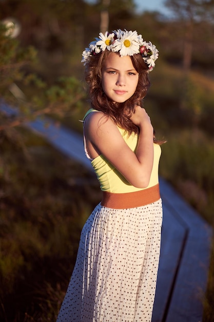 An attractive teenage girl dressed in a long skirt and garland on a head posing in the field at sunrise.