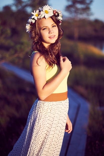 Un'adolescente attraente vestita con una gonna lunga e una ghirlanda su una testa in posa nel campo all'alba.