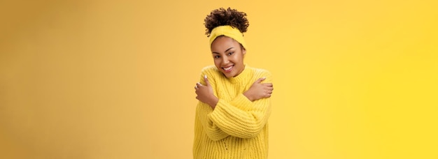 Attractive tender gentle africanamerican teenage girl in sweater headband hugging herself hands touc