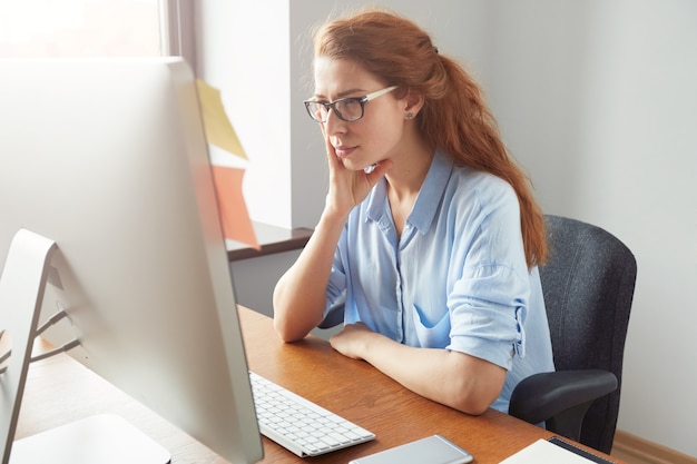 Foto gratuita attraente donna d'affari premurosa rossa guardando lo schermo con espressione concentrata