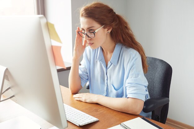 Attractive thoughtful redhead businesswoman looking at the screen with concentrated expression