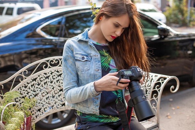 카메라와 함께 매력적인 관광 여성 사진 작가, 야외 도시 거리. 캐주얼 힙스터 옷을 입은 화려한 행복한 백인 여성