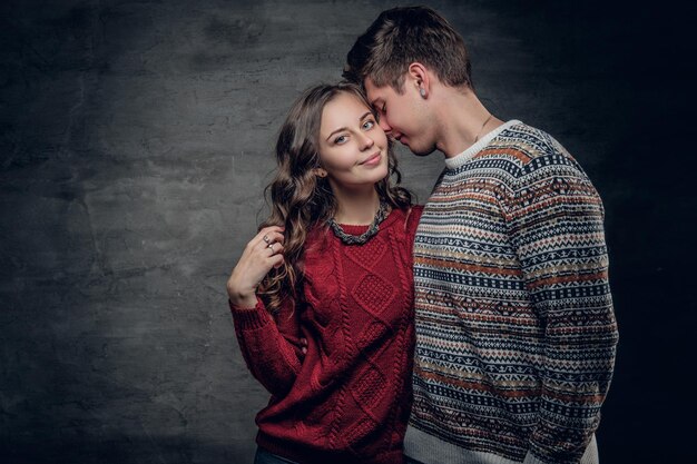 Attractive urban couple in warm autumn sweaters posing in a studio on grey background.