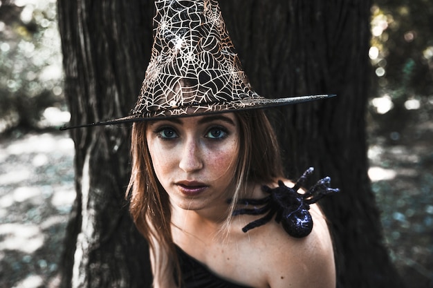 Attractive witch with spider on shoulder in forest datime