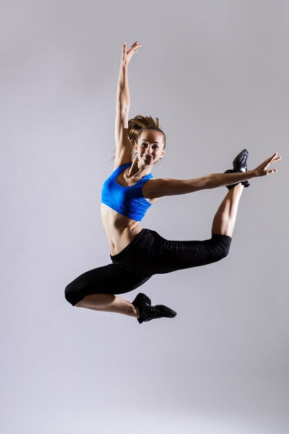 Attractive woman in aquamarine sportswear with ponytail working out on gray background