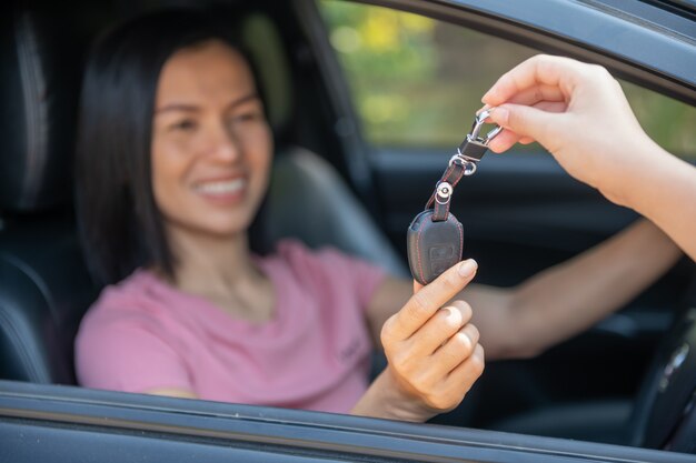 車の中で魅力的な女性が車の鍵を受け取ります。自動車のレンタルまたは購入 – コンセプト。カーディーラーで顧客と仕事をしているプロの販売員。新しい車の所有者に鍵を渡します。