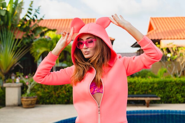 재미, 스포츠 패션 스타일을 갖는 감정적 인 얼굴 표정 미소 여름 휴가에 선글라스를 쓰고 화려한 분홍색 까마귀에 매력적인 여자