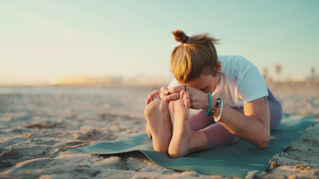 Привлекательная женщина занимается йогой на открытом воздухе Учитель йоги упражняется на коврике, растягивая тело во время утренней йоги на пляже