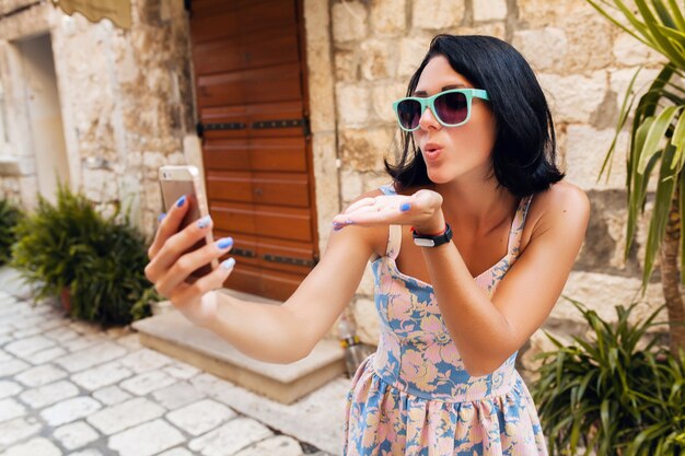 Attractive woman in dress treveling on vacation in old city center of Italy making selfie funny photo on phone sending kiss