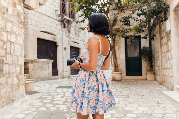 Attractive woman in dress treveling on vacation in old city center of Italy taking pictures on camera