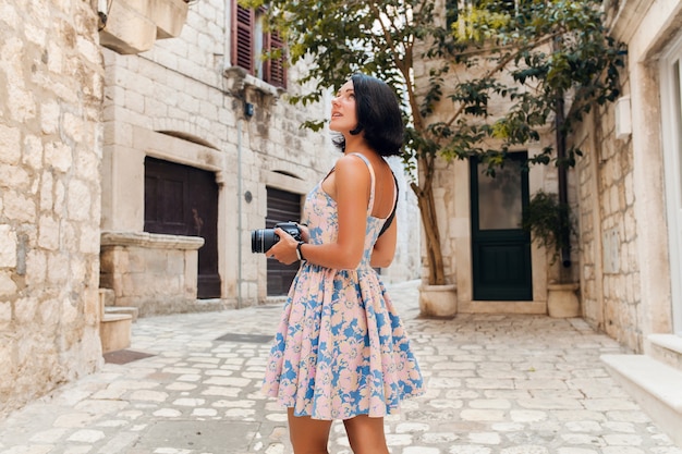 カメラで写真を撮るイタリアの旧市街中心部で休暇中にトレベリングドレスを着た魅力的な女性