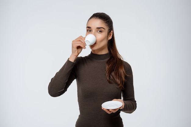 Donna attraente che beve caffè, tenendo la tazza di caffè espresso