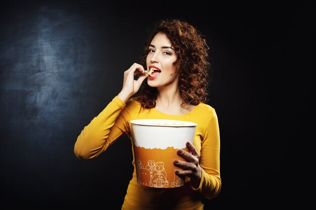 Attractive woman eating cheesy popcorn looking pleased and happy