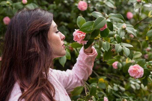 魅力的な女性は緑の小枝に成長しているピンクの花を保持