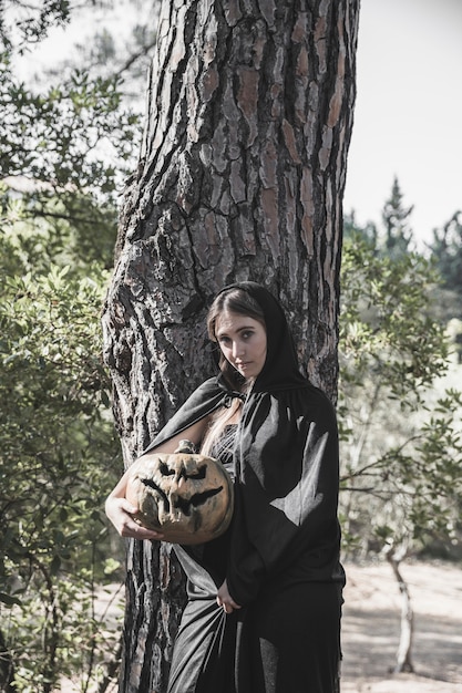 Free photo attractive woman holding pumpkin and suit, leaning on tree