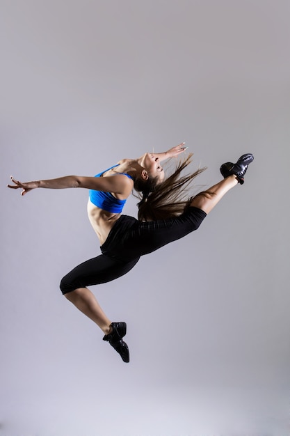 Бесплатное фото Привлекательная женщина в спортивной одежде цвета морской волны с хвостиком, тренирующимся на сером фоне