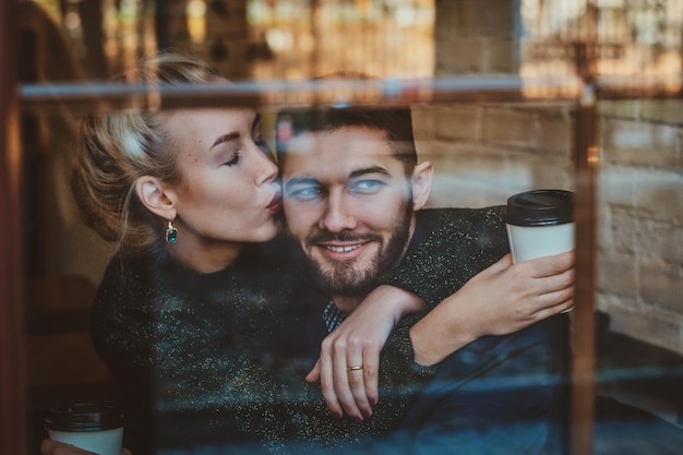 魅力的な女性がコーヒーを飲みながらカフェに座っている間、彼女の男にキスをしています。