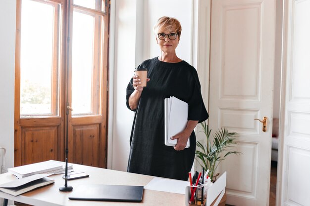 Attractive woman in oversized dress poses with cup of tea