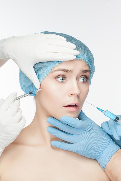 白い背景の上の彼女の顔に注射器で整形手術で魅力的な女性