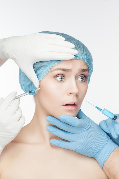 Attractive woman at plastic surgery with syringe in her face on white background