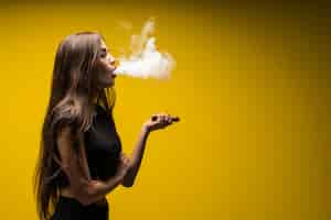 Free photo attractive woman standing and vaping on yellow wall.