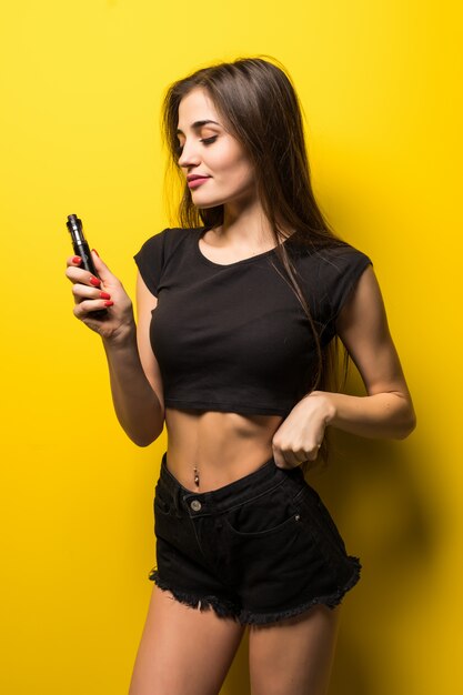 Attractive woman standing and vaping on yellow wall.