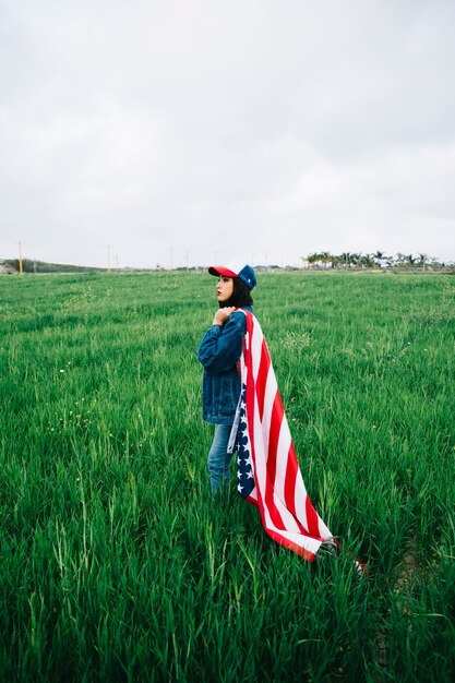 Attractive woman staying in summer field with flag