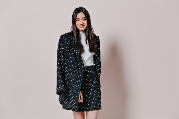 Attractive woman in suit in polka dot smiles on beige wall