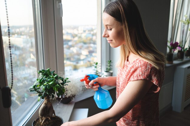 Attractive woman watering a bonsai tree in the apartment