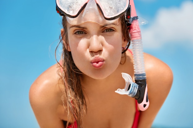 Free photo attractive woman wears snorkel scuba mask, swims in ocean or sea, likes diving, enjoys summer holidays, poses against blue sky