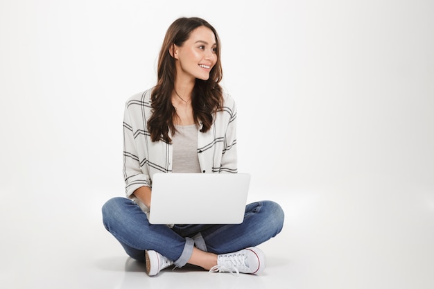 아름 다운 미소 로터스에 앉아 매력적인 여자 실버 노트북을 사용 하 고 멀리보고, 흰 벽 위에 절연 바닥에 포즈