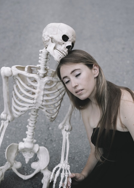 Attractive woman with close eyes sitting on asphalt with decorative skeleton of man