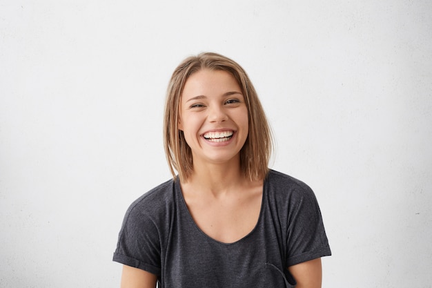 Free photo attractive woman with short fair hair being very glad smiling with broad smile showing her perfect teeth having fun indoors. joyful excited cheery woman rejoicing