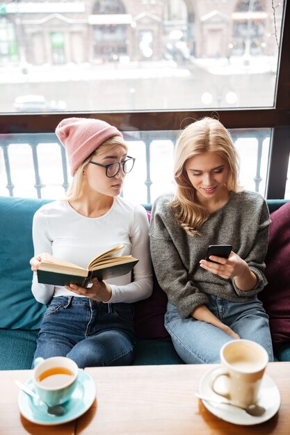 Attractive women in cafe reading book while using phone.