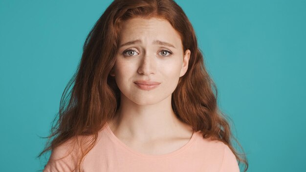 Attractive worry redhead girl sadly looking in camera over colorful background