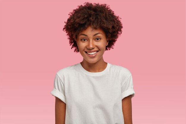 歯を見せる優しい笑顔で魅力的な若いアフリカ系アメリカ人の女性は、カジュアルなモックアップTシャツを着て白い歯を示しています
