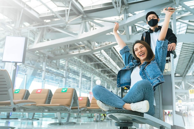 Attractive Young Asian tourist couple excited together for the trip girlfriend sitting and cheering on baggage trolley or luggage trolley Holiday vacation safety traveling abroad ideas concept