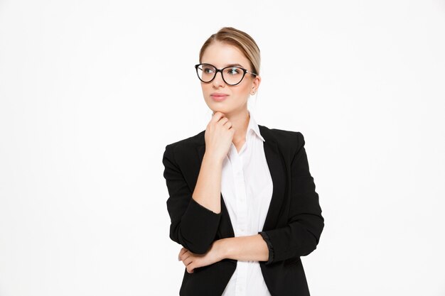 Attractive young blonde business woman in eyeglasses holding hand near chin and looking away over white 