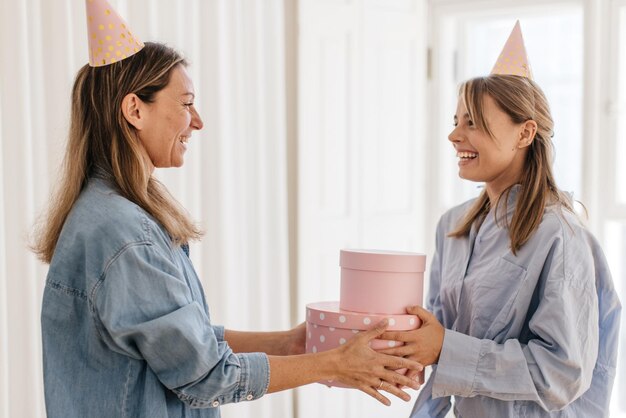 Attractive young blonde woman gives her mother gift in pink boxes on white background. Concept of enjoying moment