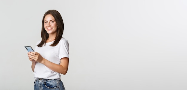 Attractive young brunette woman using mobile phone and smiling at camera