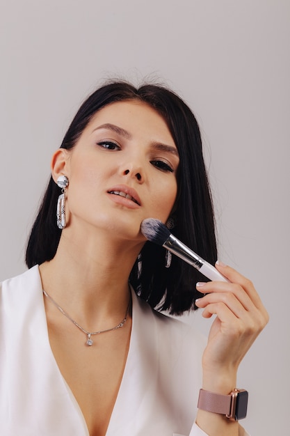 Attractive young business girl with makeup brushes posing on plain background. concept of makeup and cosmetics.