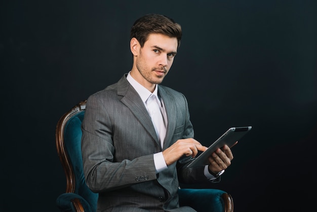 Привлекательный молодой бизнесмен, сидя в кресле, используя цифровой планшет