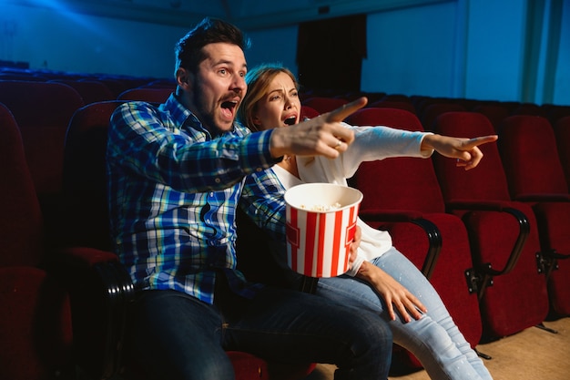 Attractive young caucasian couple watching a film at a movie theater, house or cinema. Look expressive, astonished and emotional. Sitting alone and having fun. Relation, love, family, weekend time.