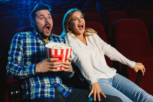 영화 극장, 집 또는 영화관에서 영화를보고 매력적인 젊은 백인 부부. 표현력이 풍부하고 놀랍고 감정적으로 보입니다. 혼자 앉아서 즐겁게 지내기. 관계, 사랑, 가족, 주말 시간.