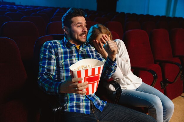 Attractive young caucasian couple watching a film at a movie theater, house or cinema. Look expressive, astonished and emotional. Sitting alone and having fun. Relation, love, family, weekend time.