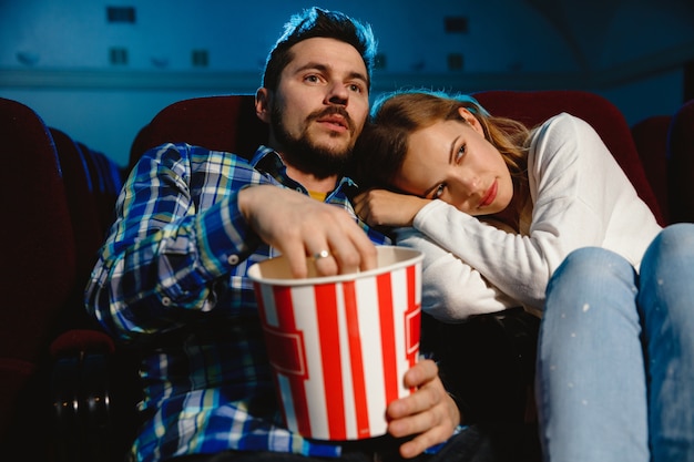 Attractive young caucasian couple watching a film at a movie theater, house or cinema. Look expressive, astonished and emotional. Sitting alone and having fun. Relation, love, family, weekend time.